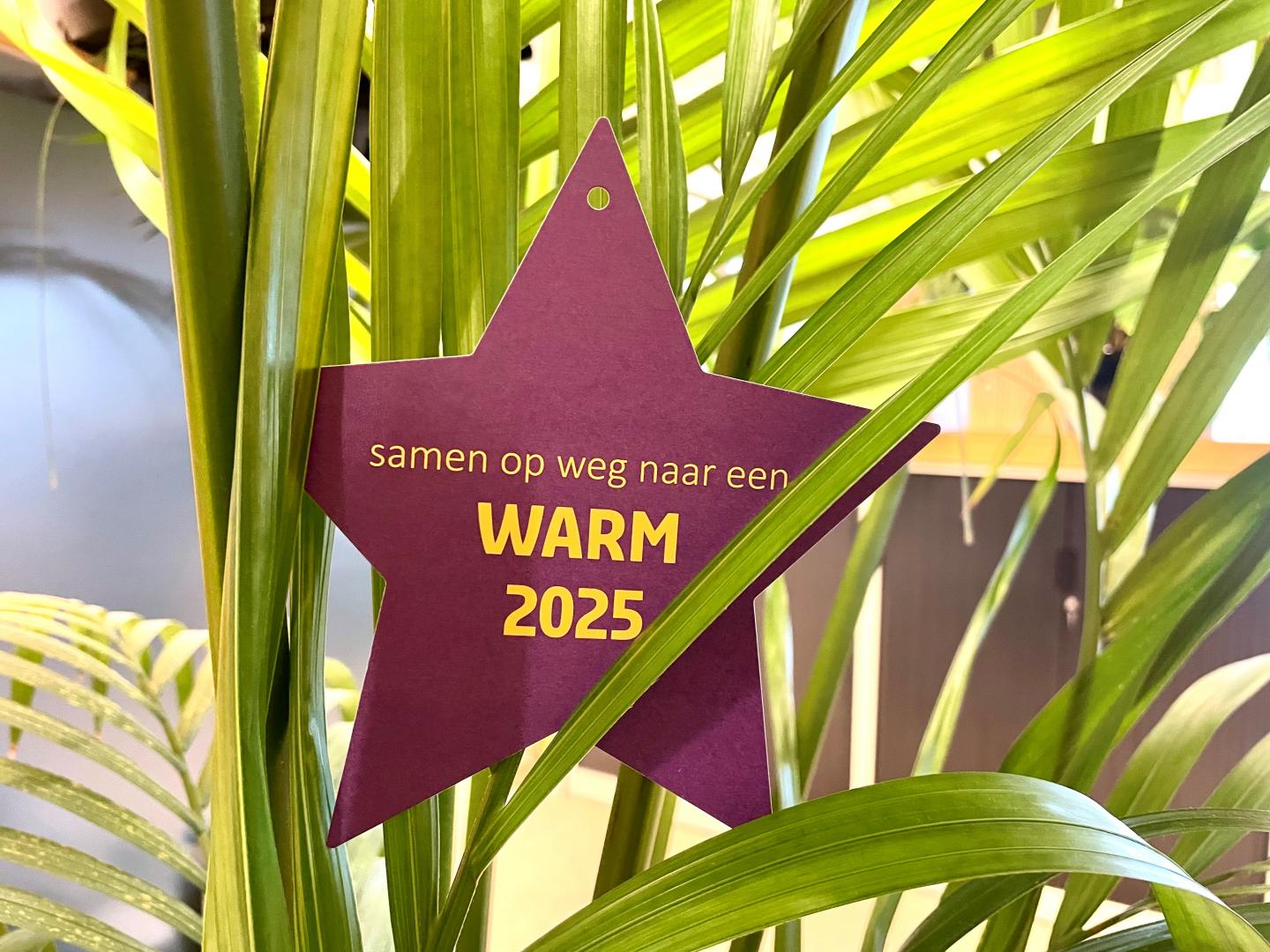 Ster met 'samen op weg naar een warm 2025' opgehangen in een plant